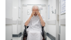 Man in wheelchair and hospital gown holding head in hands